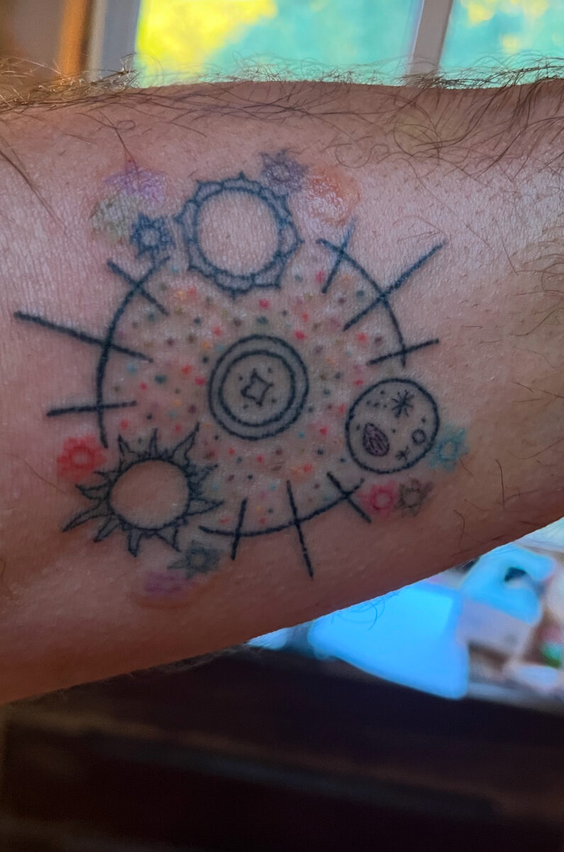 Seeds, suns, and blooms mandala tattoo on Yanik's left arm